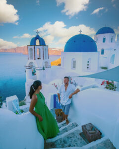 Santorini Greece, a young couple on luxury vacation at the Island of Santorini watching the sunrise by the blue dome church and whitewashed village of Oia Santorini Greece